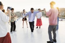 Group of young Japanese men and women dancing on rooftop in urban setting. — Stock Photo