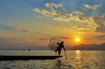 Pêcheur traditionnel se balançant sur une jambe à bord d'un bateau, tenant un panier de pêche, pêchant sur le lac Inle au coucher du soleil, Myanmar. — Photo de stock