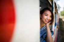 Sorridente giovane donna in sella a un treno, guardando fuori dalla finestra. — Foto stock