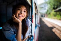 Sorridente giovane donna in sella a un treno, guardando fuori dalla finestra. — Foto stock