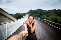 Усміхнена молода жінка стоїть на мосту, тримаючи чоловічу руку . — стокове фото