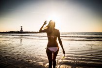 Vista vertical de la mujer que camina hacia la playa durante la puesta de sol. - foto de stock