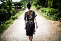Vue arrière d'une femme portant une robe de dentelle noire marchant le long d'une route rurale. — Photo de stock