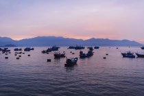Large group of fishermen in traditional fishing boats on lake at sunrise, mountains in the distance. — Stock Photo