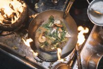Gros plan sur les frites avec crevettes et légumes verts dans un wok en acier inoxydable au-dessus de la flamme du barbecue au charbon de bois . — Photo de stock