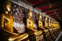 Primer plano de una fila de estatuas doradas de Buda a lo largo de una pared, Wat Suthat, Tailandia - foto de stock