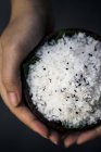 High angle close-up of hands holding bowl of coconut and black sesame seeds body scrub. — Stock Photo
