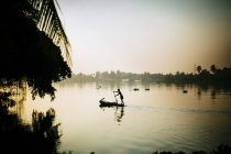 Местный рыбак гребёт на лодке по реке рано утром, Вьетнам — стоковое фото