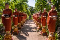 Reihen buddhistischer Mönchsstatuen mit roten Gewändern und Almosenschalen im Garten des buddhistischen Tempels in siem reap, Kambodscha — Stockfoto