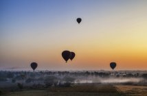 Balões de ar quente sobre a paisagem com templos distantes ao pôr do sol, Bagan, Myanmar . — Fotografia de Stock