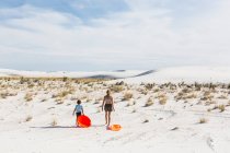 Niños con trineos y dunas de arena trepadora, Monumento Nacional de las Tierras Blancas, NM. - foto de stock