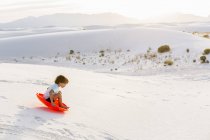 6-летний мальчик катается на санках по дюнам, Белые пески, штат Нью-Мексико — стоковое фото