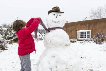 Niño de seis años que construye un hombre de nieve - foto de stock