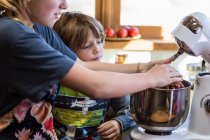 Trece años de edad adolescente y su hermano de 6 años en la cocina utilizando un tazón de mezcla. - foto de stock