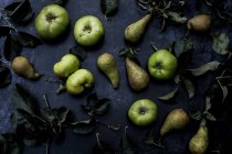 High angle close up of green pears and Bramley apples on black background. — Stock Photo