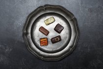 High angle close up of a selection of chocolate pralines on a tin plate on black background. — Stock Photo