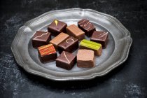 Hohe Nahaufnahme einer Auswahl von Schokoladenpralinen auf einem Zinnteller auf schwarzem Hintergrund. — Stockfoto