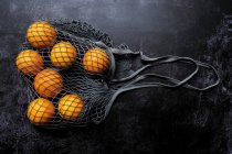 Alto ângulo perto de laranjas em saco de rede cinza no fundo preto . — Fotografia de Stock