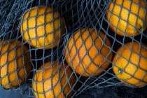 High angle close up of oranges in grey net bag on black background. — Stock Photo