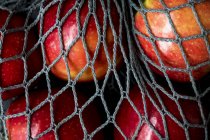 High angle close up of red apples in grey net bag on black background. — Stock Photo