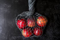High angle close up of red apples in grey net bag on black background. — Stock Photo
