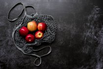 Alto angolo primo piano di mele rosse in borsa a rete grigia su sfondo nero . — Foto stock