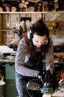 Woman with long brown hair wearing dungarees, safety glasses and ear protectors standing in wood workshop, using sander. — Stock Photo