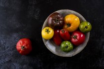 High angle close up of grey plate with selection of tomatoes in various shapes and colours on black background. — Stock Photo