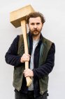 Portrait of bearded man holding wooden block standing in front of white background, looking at camera. — Stock Photo