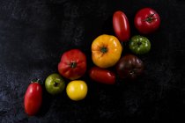 High angle close up of a selection of tomatoes in various shapes and colours on black background. — Stock Photo