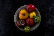Alto angolo di chiusura della piastra grigia con selezione di pomodori in varie forme e colori su fondo nero . — Foto stock