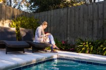 Mulher sentada na espreguiçadeira junto a uma piscina — Fotografia de Stock