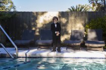 Niño de 6 años con traje negro y corbata de arco junto a una piscina. - foto de stock