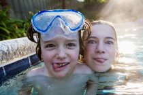 Une adolescente et son frère dans une piscine chaude, regardant la caméra, sortant leur langue. — Photo de stock