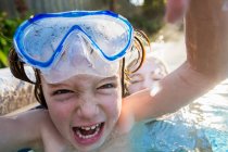 Boy in goggles laughing at the camera, in a warm swimming pool with his sister. — Stock Photo