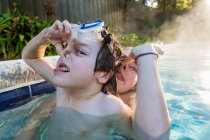 Boy and his sister playing in pool in early morning light, boy holding his nose. — Stock Photo