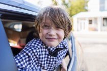 Un niño de seis años sonriendo en la cámara, mirando desde la ventana del coche. - foto de stock