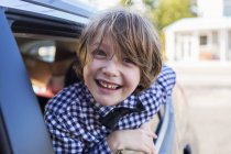 Six year old boy smiling at camera, looking out of car window — Stock Photo