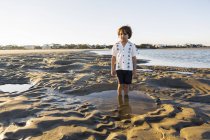 Un garçon de six ans debout dans une piscine peu profonde sur le sable — Photo de stock