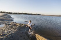 Menino de seis anos na praia espirrando em águas rasas — Fotografia de Stock