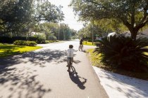 Niños, adolescentes y su hermano que van en bicicleta por una carretera suburbana. - foto de stock