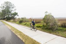 Joven adolescente montando una bicicleta a lo largo de un sendero en tierra abierta por el agua, Isla de San Simón, Georgia. - foto de stock