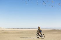 Teenage girl cycling on sand towards a flock of seagulls, St. Simon's Island, Georgia — Stock Photo