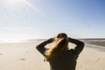 Une adolescente se tient debout sur une grande plage ouverte, regardant au loin. — Photo de stock