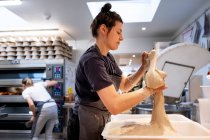 Femme portant un tablier debout dans une boulangerie artisanale, travaillant avec du levain . — Photo de stock