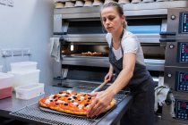 Женщина в фартуке, стоящая в ремесленной пекарне, готовит пиццу, чтобы попасть в духовку. . — стоковое фото