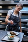 Donna che indossa grembiule in piedi in una panetteria artigianale, preparare piatto di cibo . — Foto stock