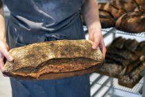 Высокий угол съемки лица, держащего свежеиспеченный хлеб в пекарне . — стоковое фото