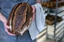 Высокий угол съемки лица, держащего свежеиспеченный хлеб в пекарне . — стоковое фото