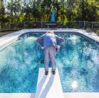 Niño de 6 años parado en el trampolín con vistas a la piscina - foto de stock